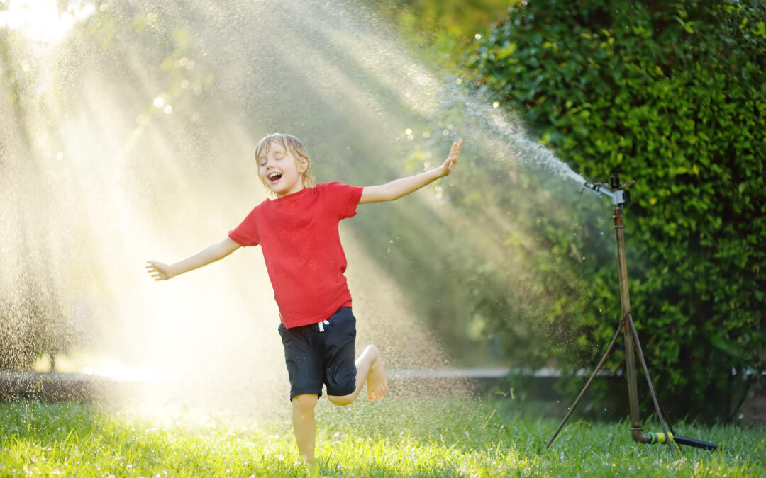 Young boy cools off by playing with a water sprinkler on a hot day in his yard.