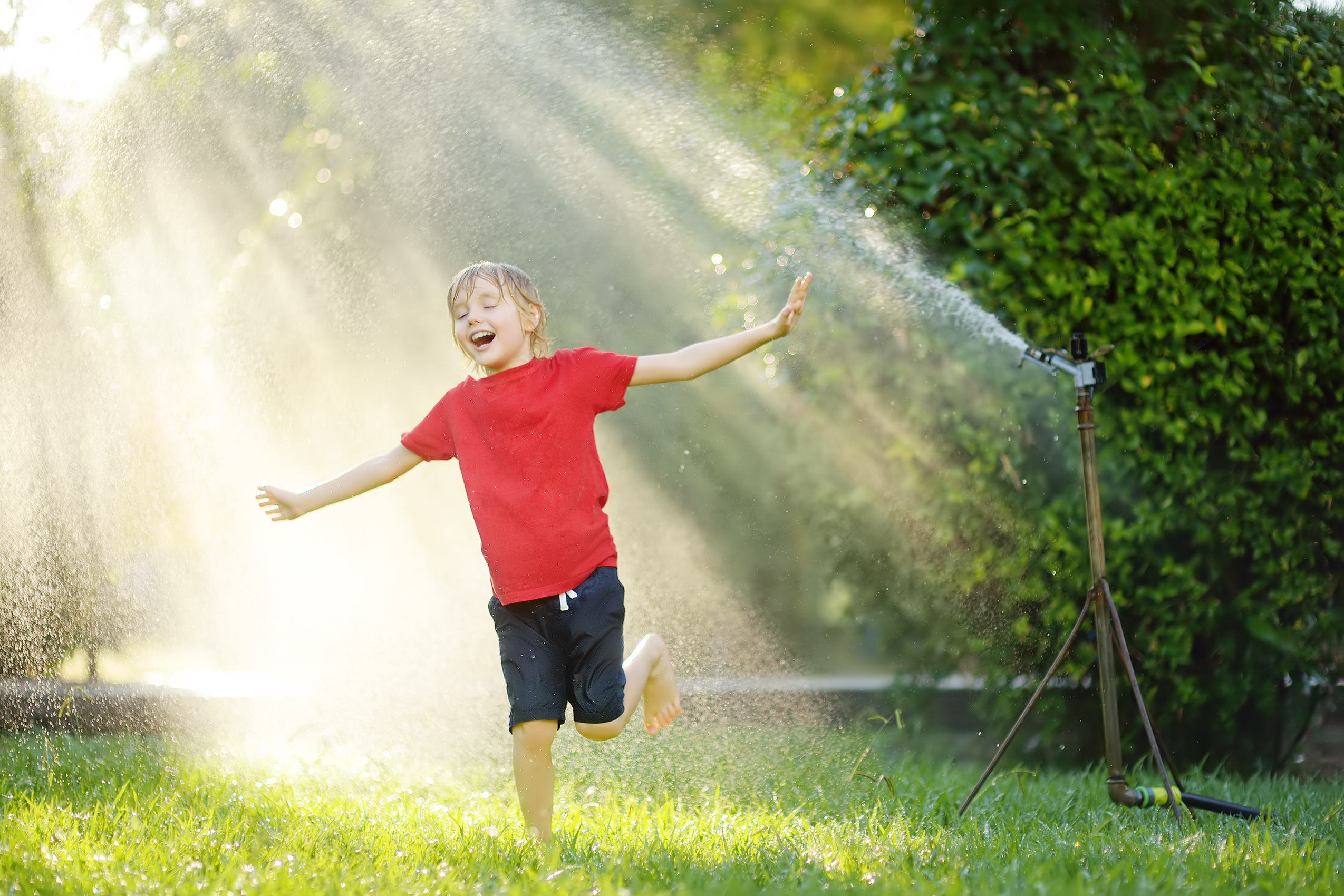 Young boy cools off by playing with a water sprinkler on a hot day in his yard.